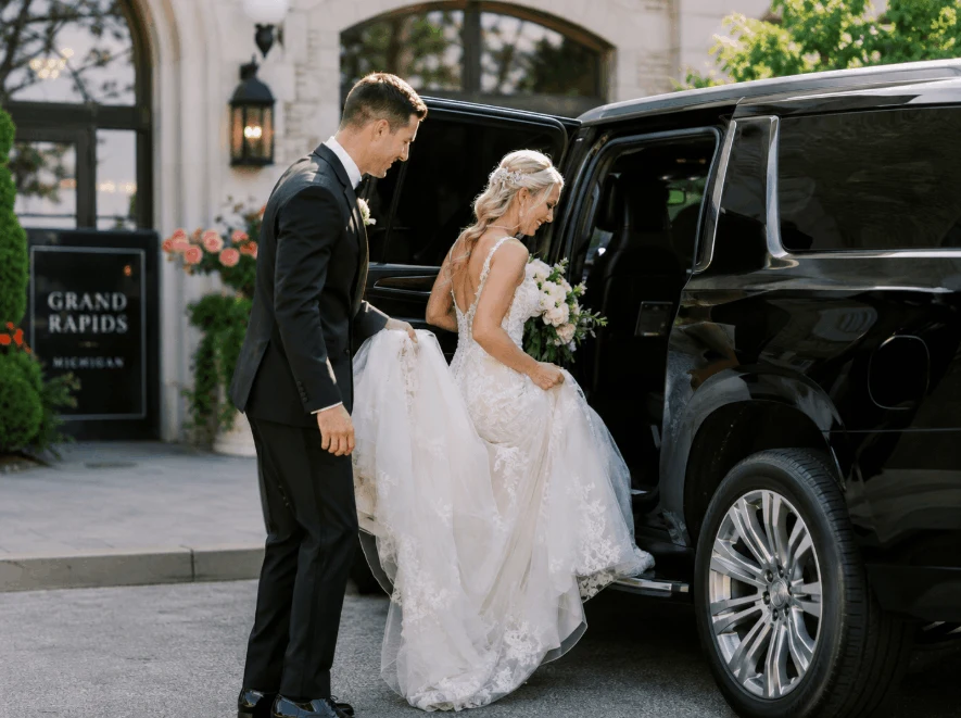 Chauffeur assisting a bride beside a black wedding SUV